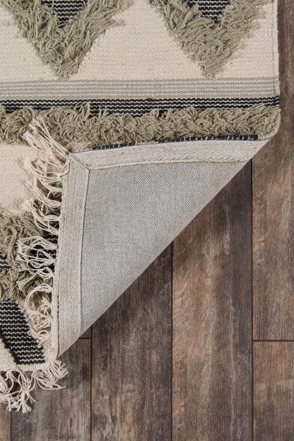 Beige and olive geometric rug with tassel fringe, folded corner shows underside on dark wood floor.