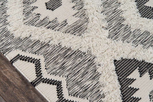 Beige and black geometric woven rug with striped texture and fluffy white fringe, modern boho accent.