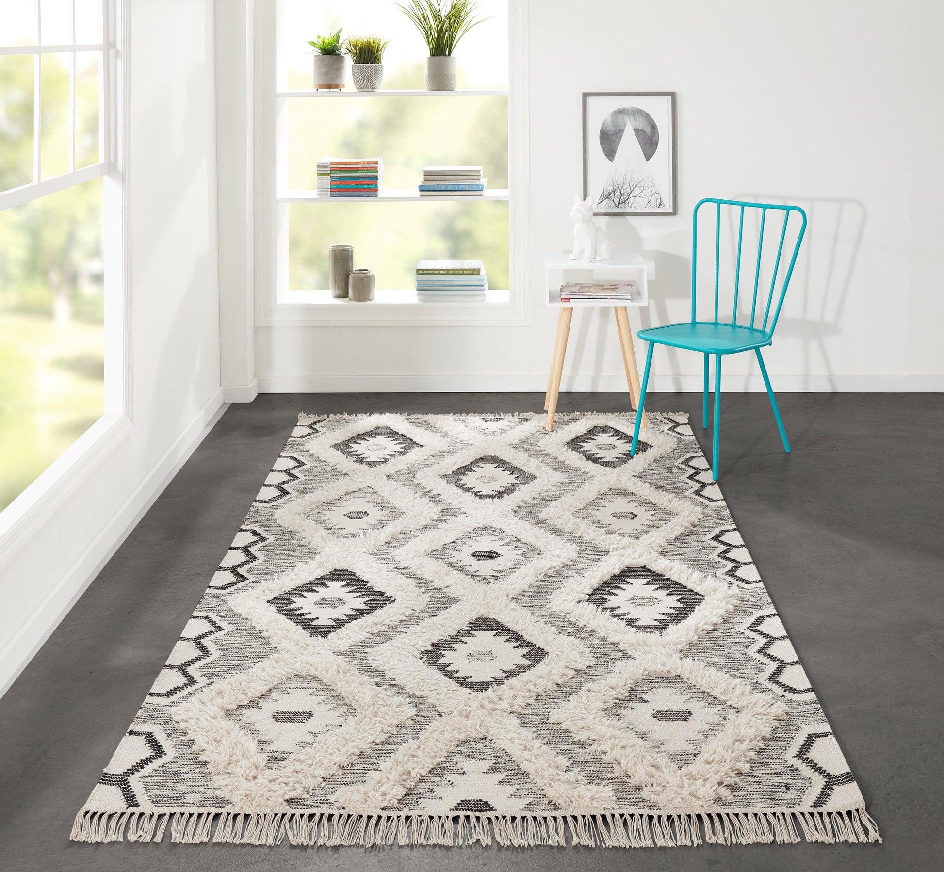 Cream and gray geometric diamond rug with fringe on a dark floor; bright room with turquoise chair, white shelves and plants.