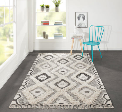 Cream and gray geometric diamond rug with fringe on a dark floor; bright room with turquoise chair, white shelves and plants.