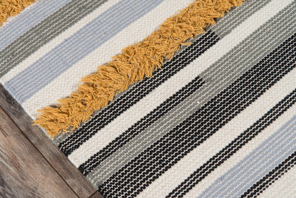 Woven striped rug with cream, black, gray, and soft blue stripes; mustard fringe along edge, on wood floor.