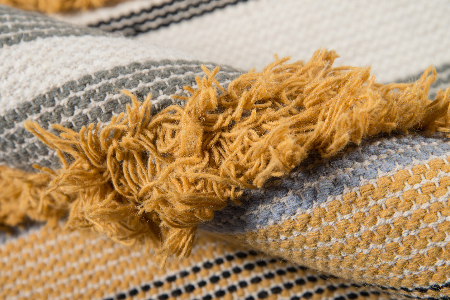 Woven rug with mustard fringe and gray and cream striped body; cozy home decor accent.