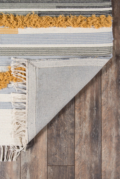 Blue, ivory and gray striped woven rug with mustard fringe, folded corner showing underside on wood floor.
