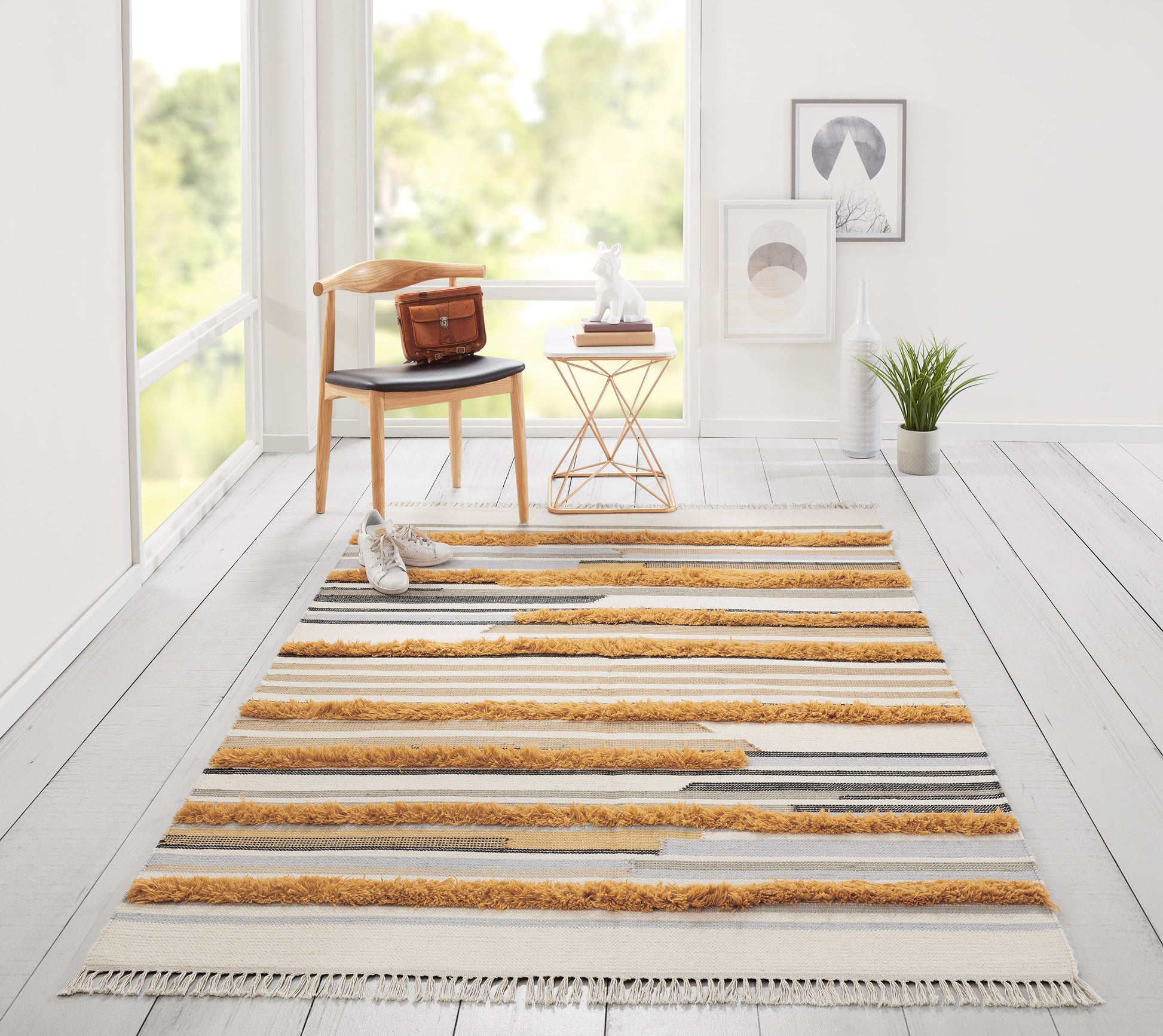 Bright room with cream striped rug and orange fringe; chair with brown bag, copper side table, plant and wall art.