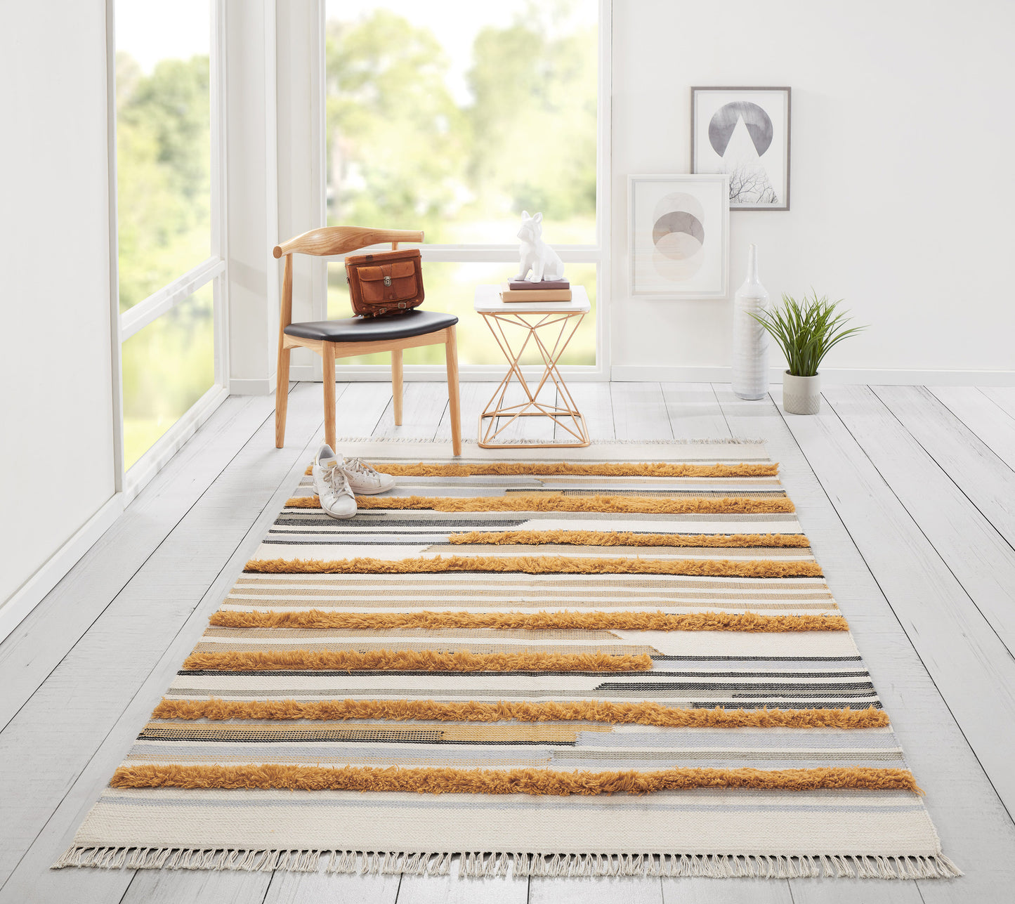 Bright living room with a long striped tufted rug in cream, gray & mustard, tasselled ends, wooden chair & small side table.