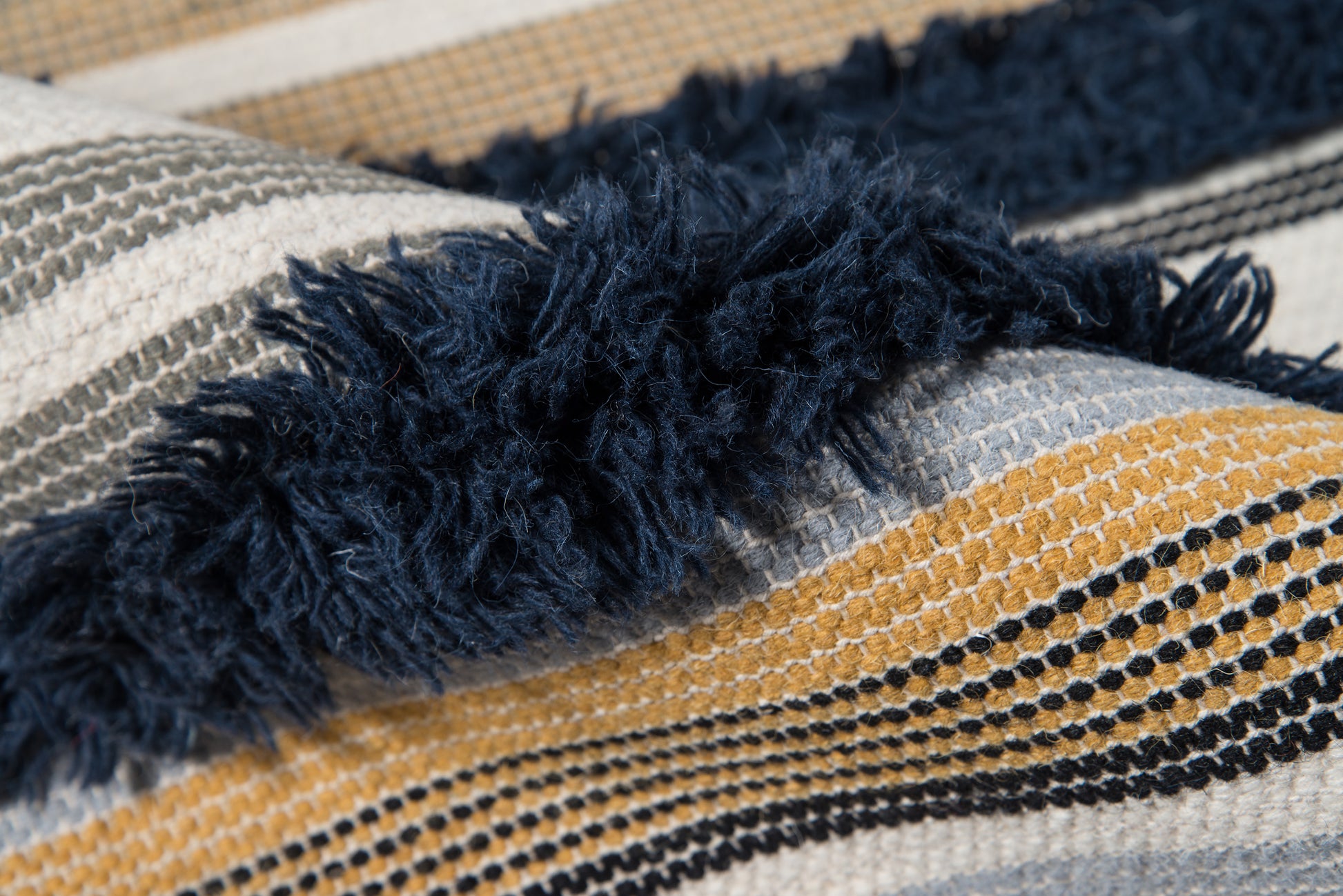 Navy fringe detail on a striped woven rug, 2' x 3'.
