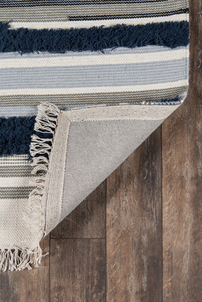 Striped woven rug in navy, light blue, gray and cream with fringed edges, folded to reveal back on a wooden floor.
