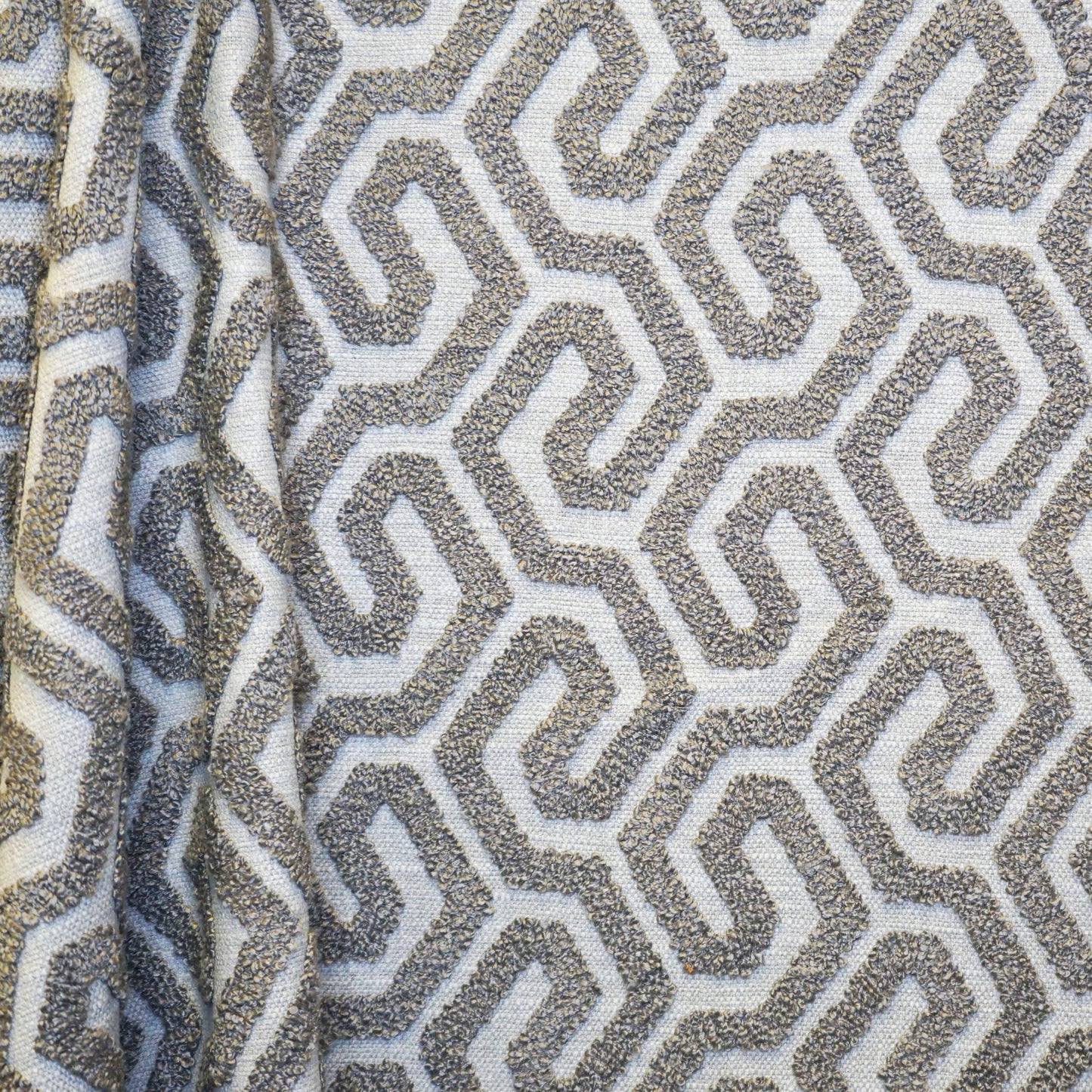 Textured woven fabric with off-white background and taupe-gray interlocking maze pattern; boucle-like raised geometric motif.