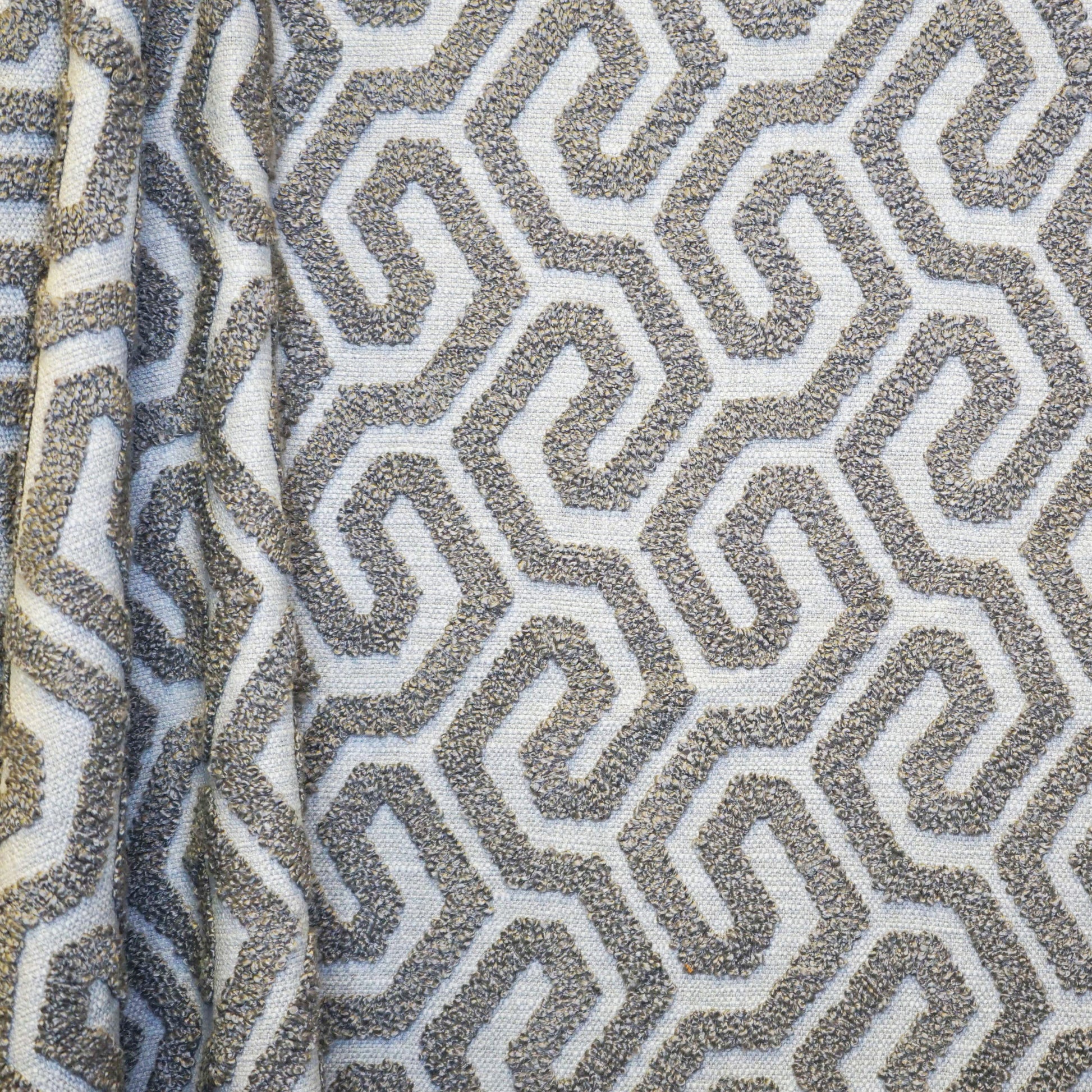 Textured woven fabric with off-white background and taupe-gray interlocking maze pattern; boucle-like raised geometric motif.