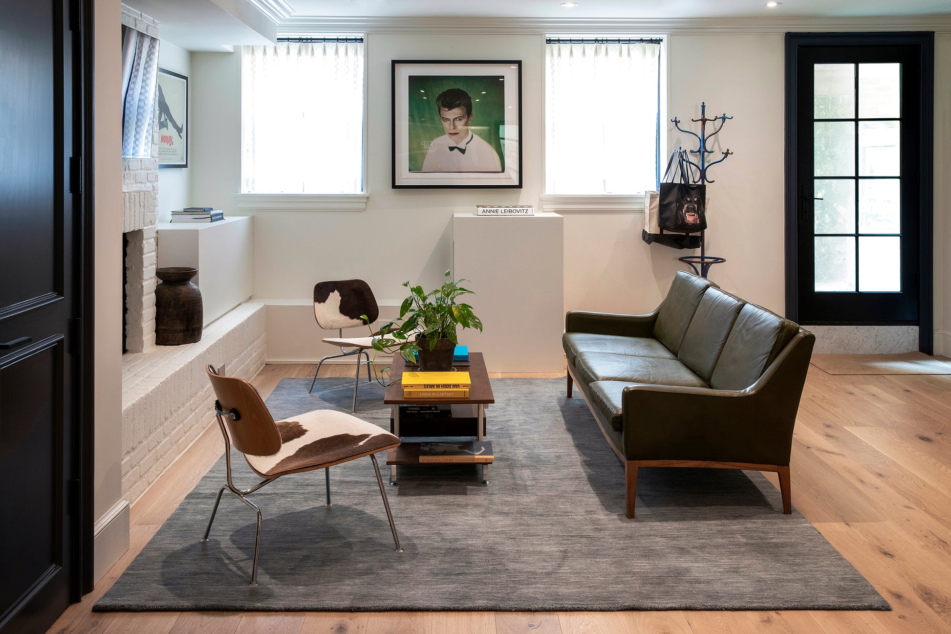 Olive-green leather sofa & wooden legs, cowhide chairs, dark wood coffee table, gray rug in a modern mid-century living room.