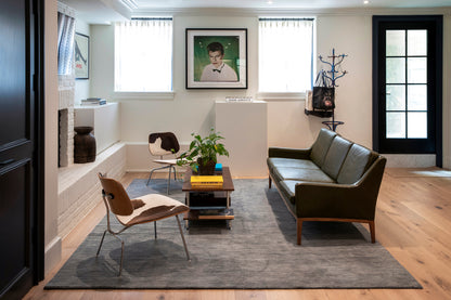 Olive-green leather sofa & wooden legs, cowhide chairs, dark wood coffee table, gray rug in a modern mid-century living room.