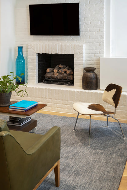 Blue-toned 2' x 8' rug runner on the floor in a cozy living room with a white brick fireplace, a plant, a cowhide chair, a green leather sofa, and a coffee table.