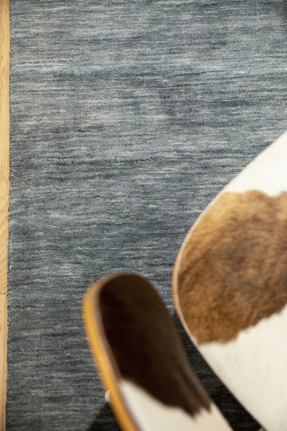 Blue-gray textured runner rug on wood floor with partial view of brown-and-white cowhide accent