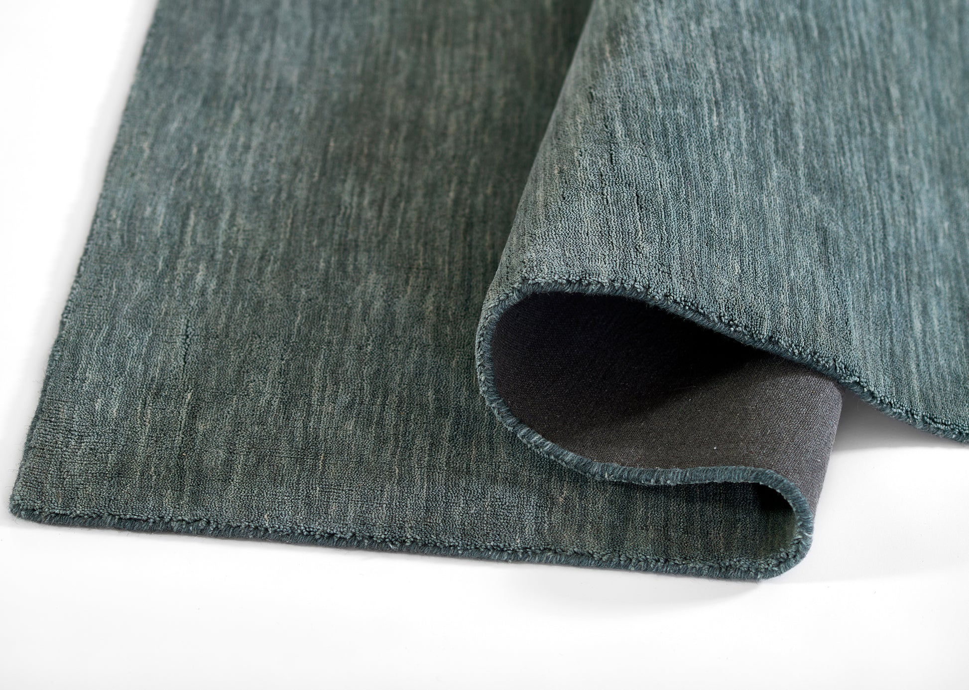 Teal-blue rectangular rug with textured loop pile and dark underside; folded corner reveals edge.