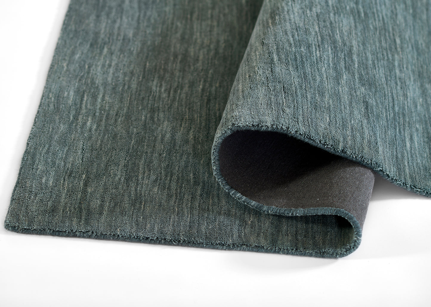 Teal blue-green rug with a soft textured pile, partially rolled at the edge, dark underside visible.