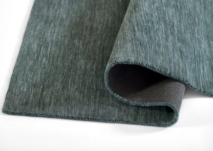 Teal-blue woven rug with bound edge and folded corner showing dark underside.