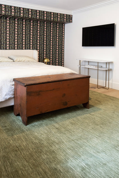 Green 2' x 8' runner rug on the floor in a bedroom with a white bed, floral curtains, green carpet, and a wall TV.