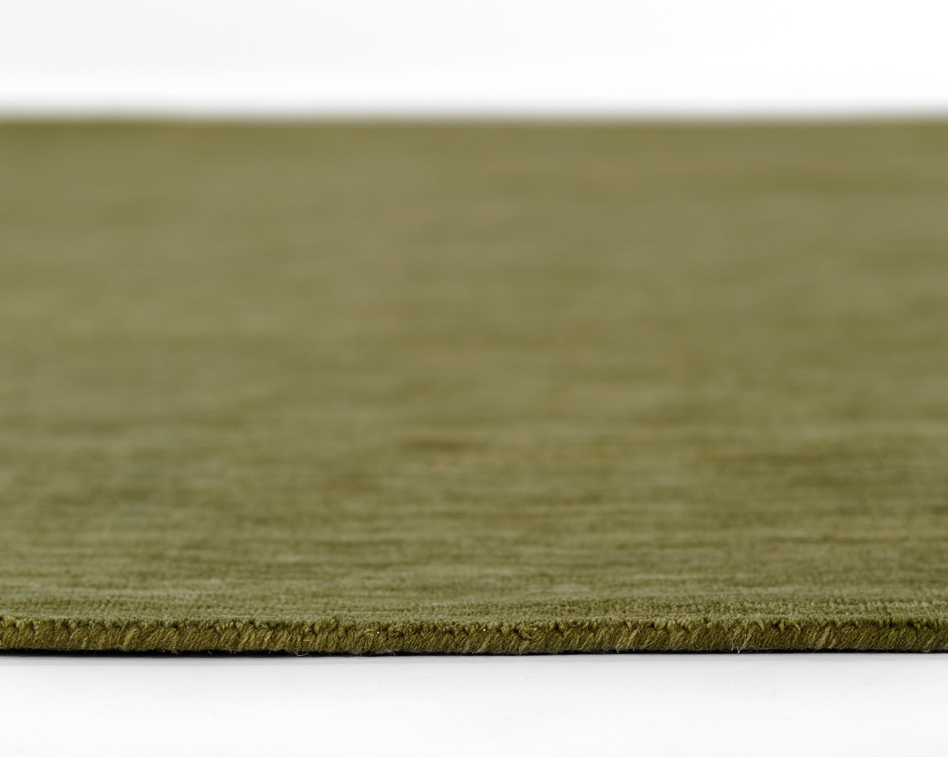 Olive green rug close-up with low-pile texture and edge fringe.