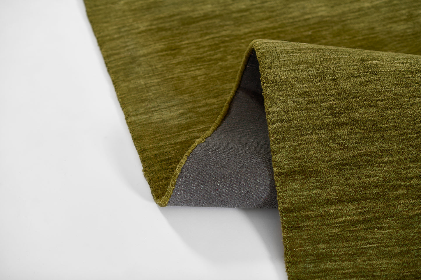 Olive green rug with a brushed texture and gray underside, edge folded to reveal the backing.