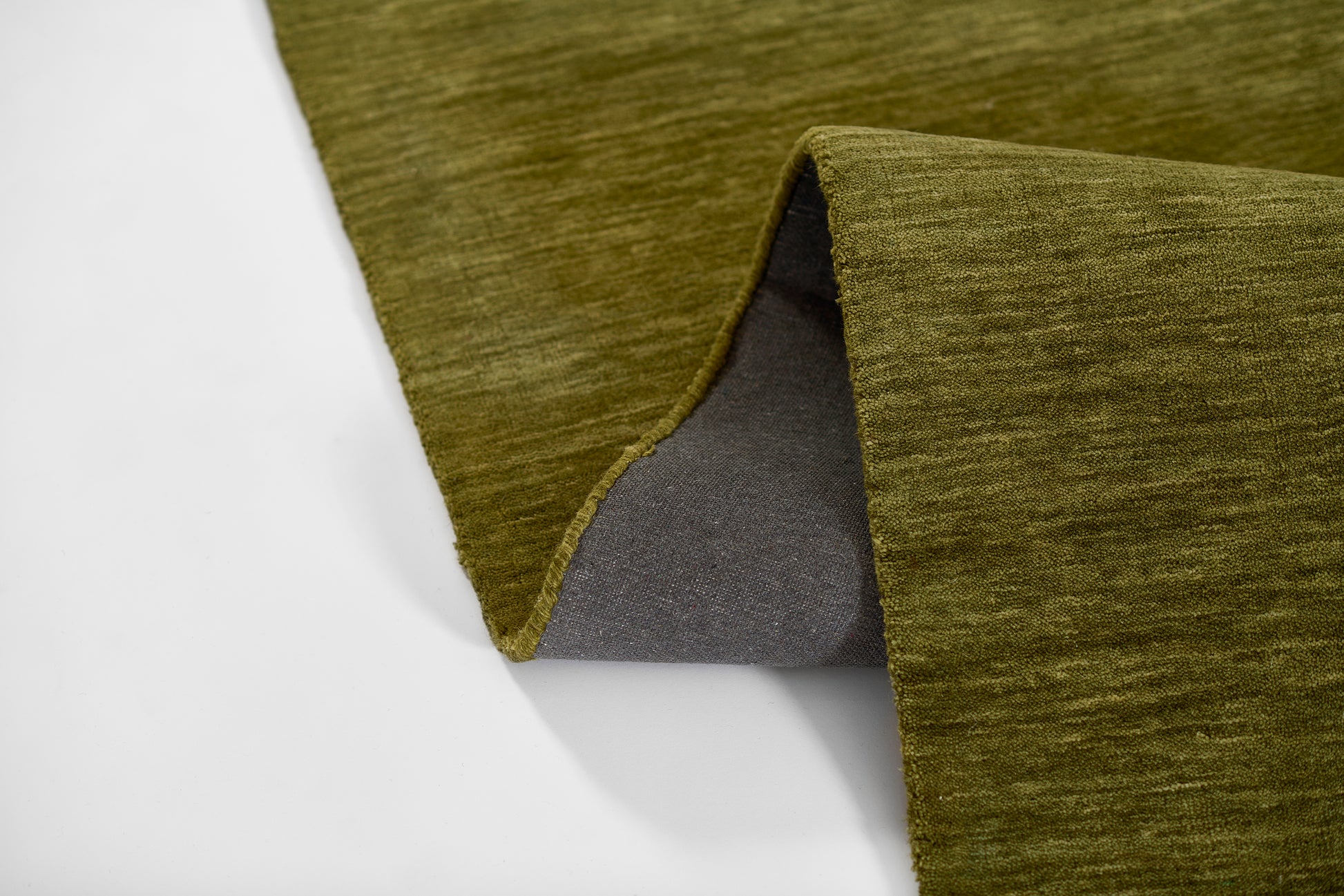 Olive green rug with a brushed texture and gray underside, edge folded to reveal the backing.