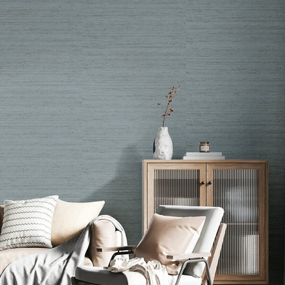 Cozy living room with light wood cabinet, glass doors, white lounge chair, beige cushions, and blue-toned textured wallpaper.