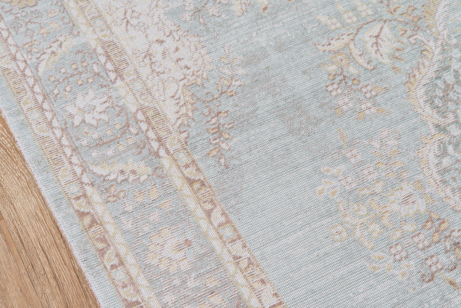 Blue and ivory patterned oriental-style rug with floral border on wooden floor.