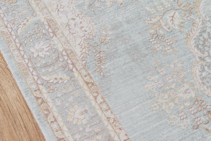 Blue and ivory patterned oriental-style rug with floral border on wooden floor.