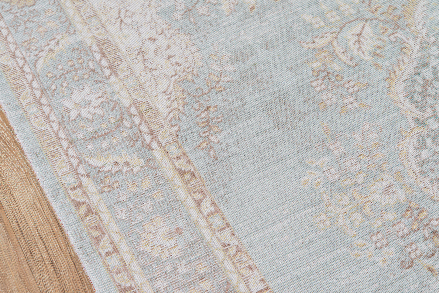 Blue-gray patterned rug with ivory floral border on a wooden floor.