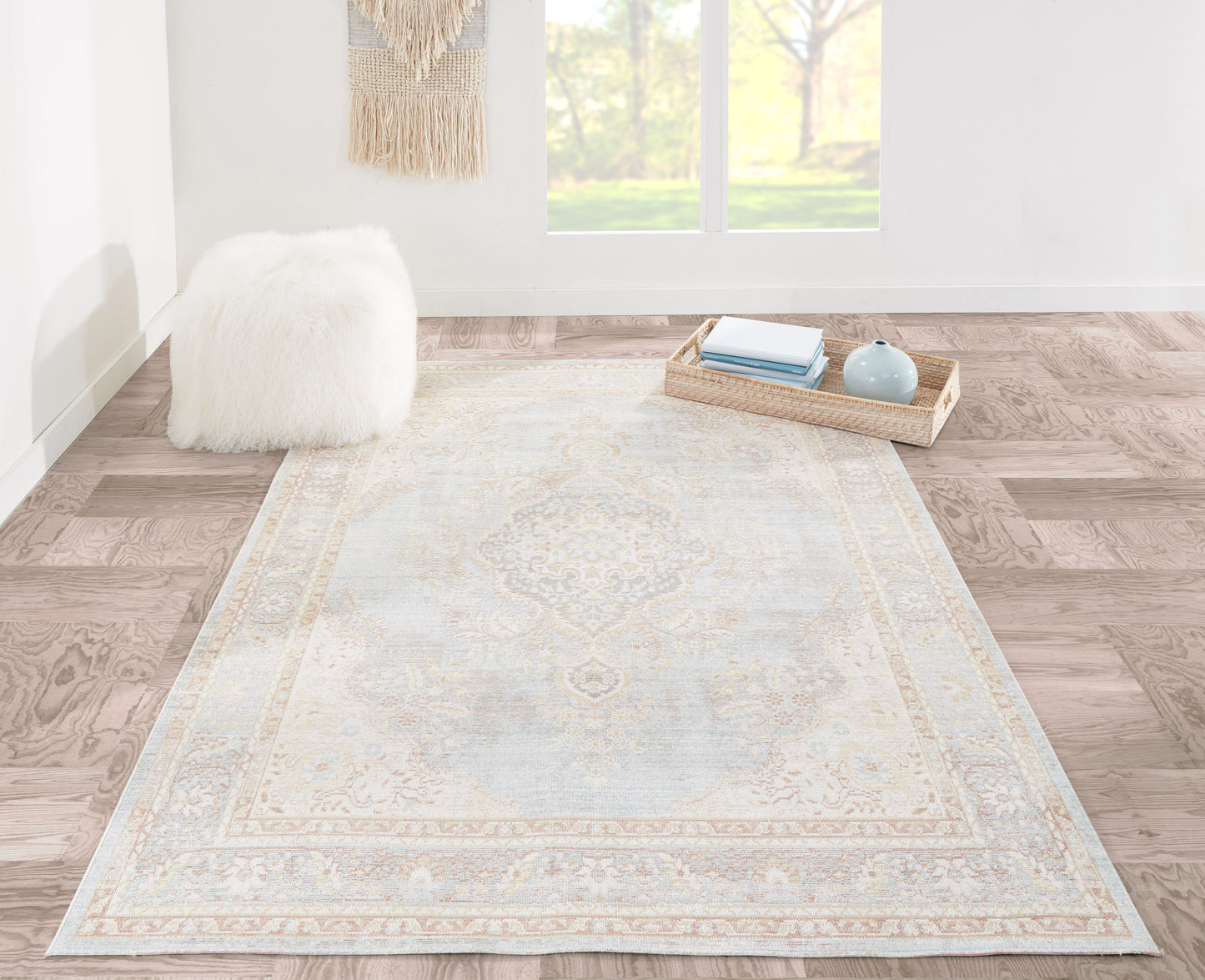 Rectangular pale blue & ivory rug with ornate pattern in a bright living room; fluffy pouf & tray with books nearby.