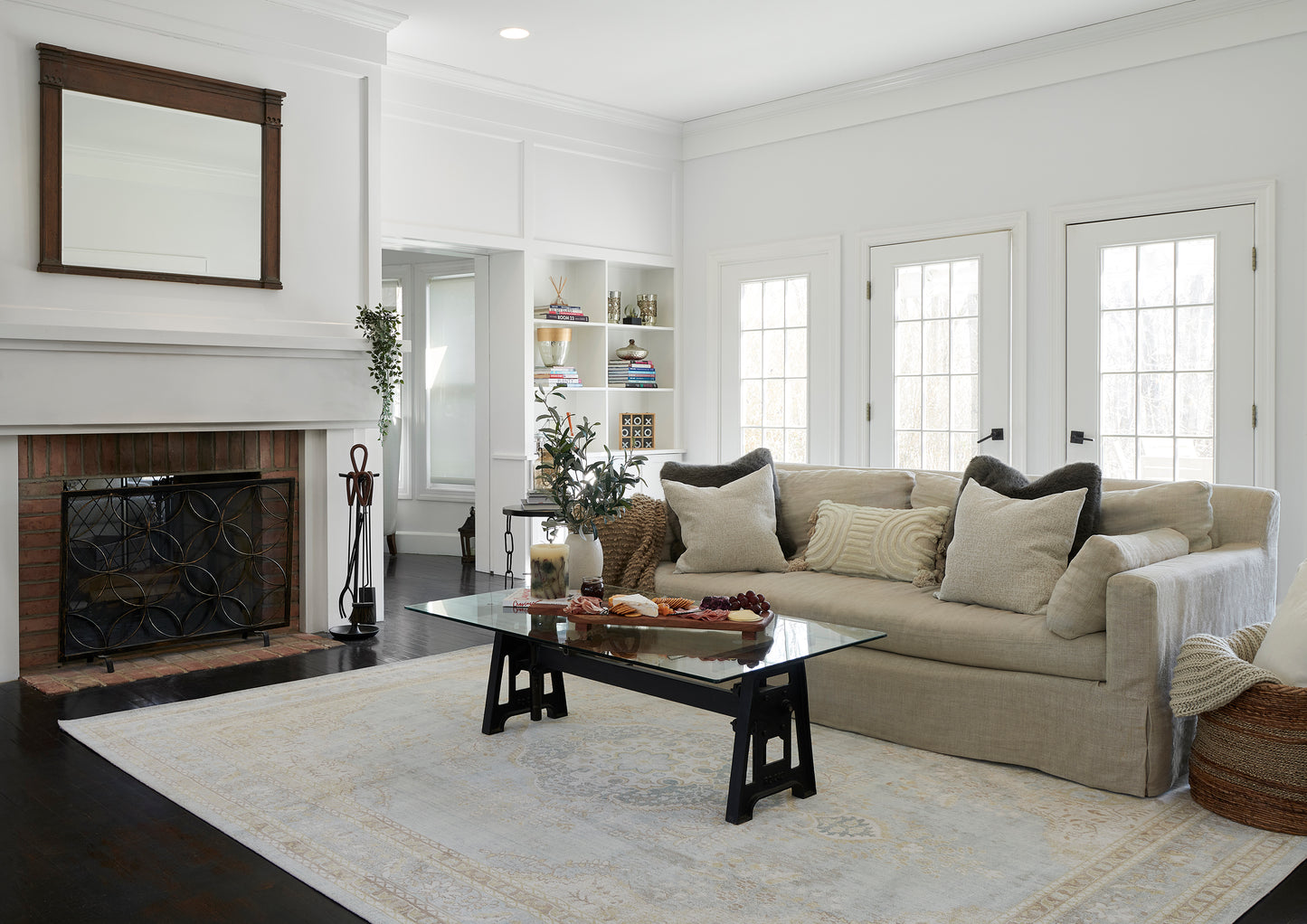 Beige patterned rug on floor in a living room scene, with a beige sofa, glass-top coffee table, white fireplace and built-in shelves.