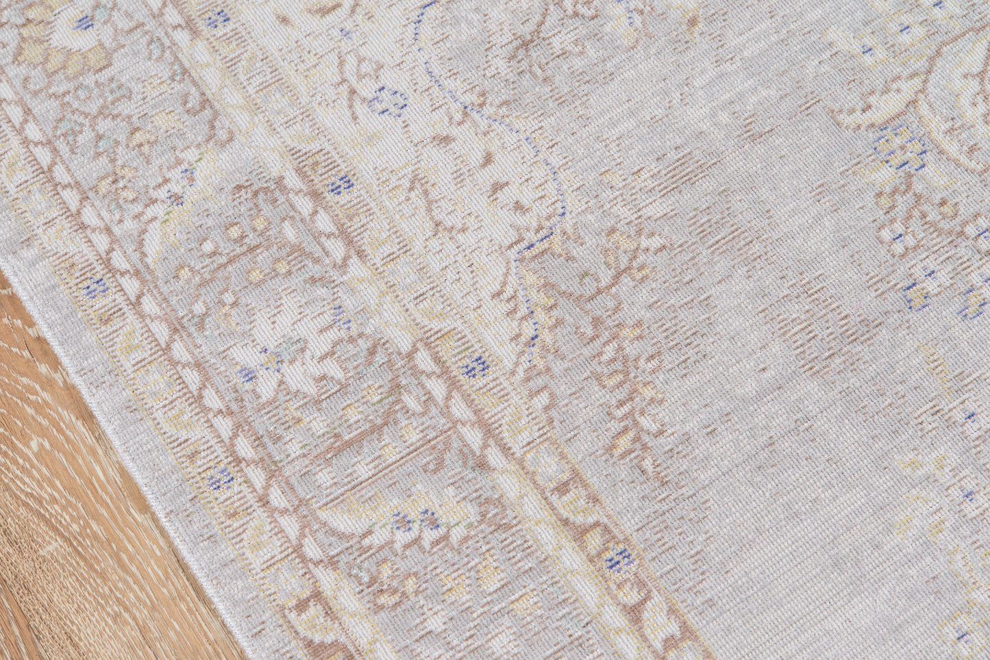 Soft gray oriental-style rug with a subtle beige and blue floral motif on a light wood floor.