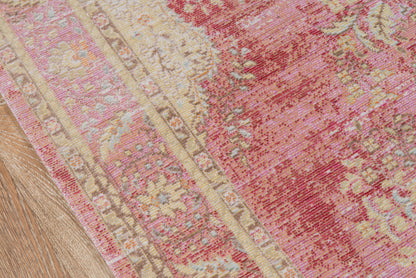 Pink and beige oriental rug with floral medallions and distressed border on wood floor.