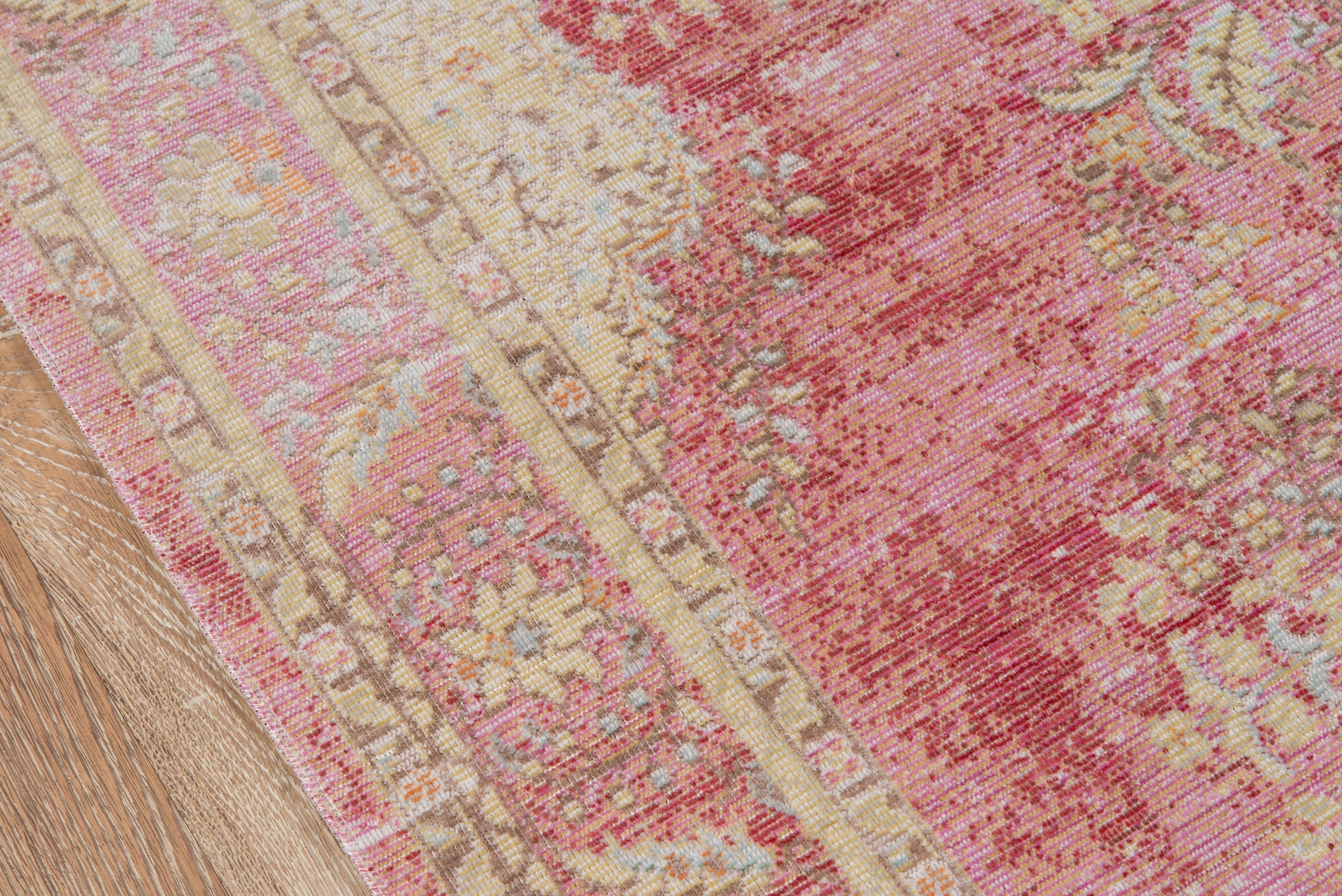 Pink floral area rug with cream/beige border on wood floor, vintage oriental style.