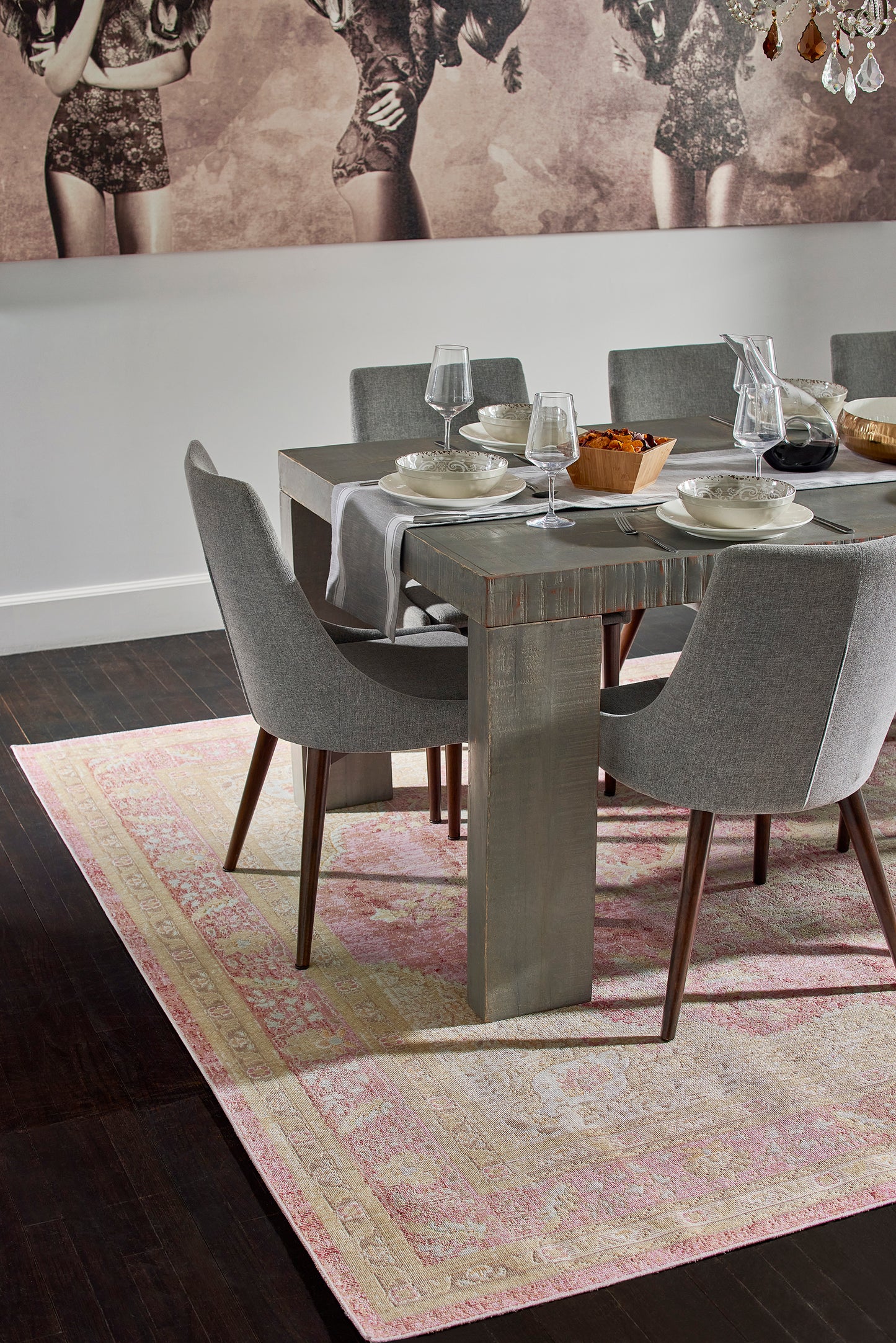 Grey patterned rug with pink accents beneath a dining table and grey upholstered chairs.