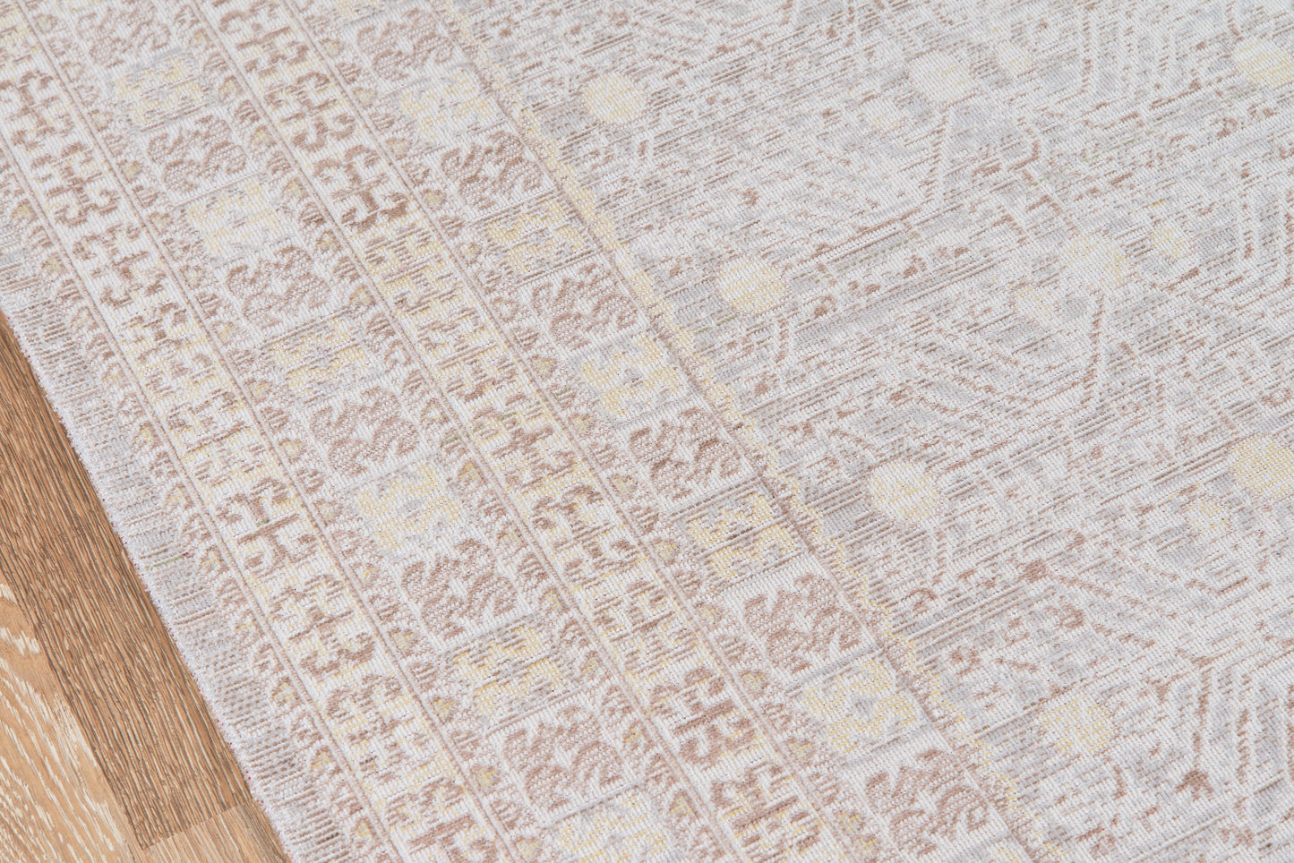 Light gray patterned area rug with subtle geometric motifs on a wooden floor, soft woven texture.