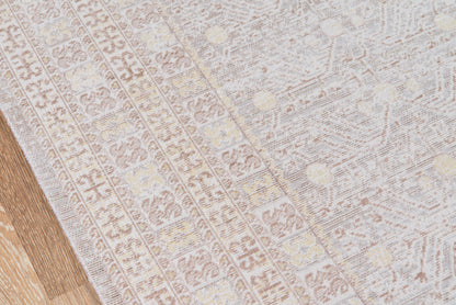 Light gray patterned area rug with subtle geometric motifs on a wooden floor, soft woven texture.
