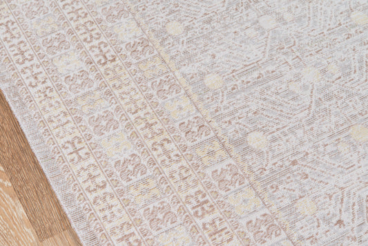 Light gray patterned area rug with subtle geometric motifs on a wooden floor, soft woven texture.