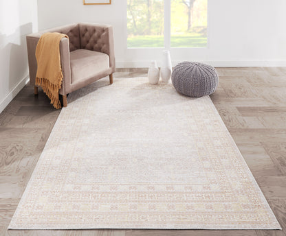 Beige-gray area rug with a subtle border in a bright living room, tan tufted chair and gray knit pouf.