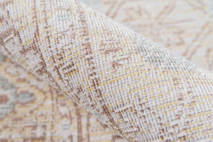 Close-up of a beige and gray-blue woven rug with subtle yellow flecks, rolled edge showing soft textured weave.