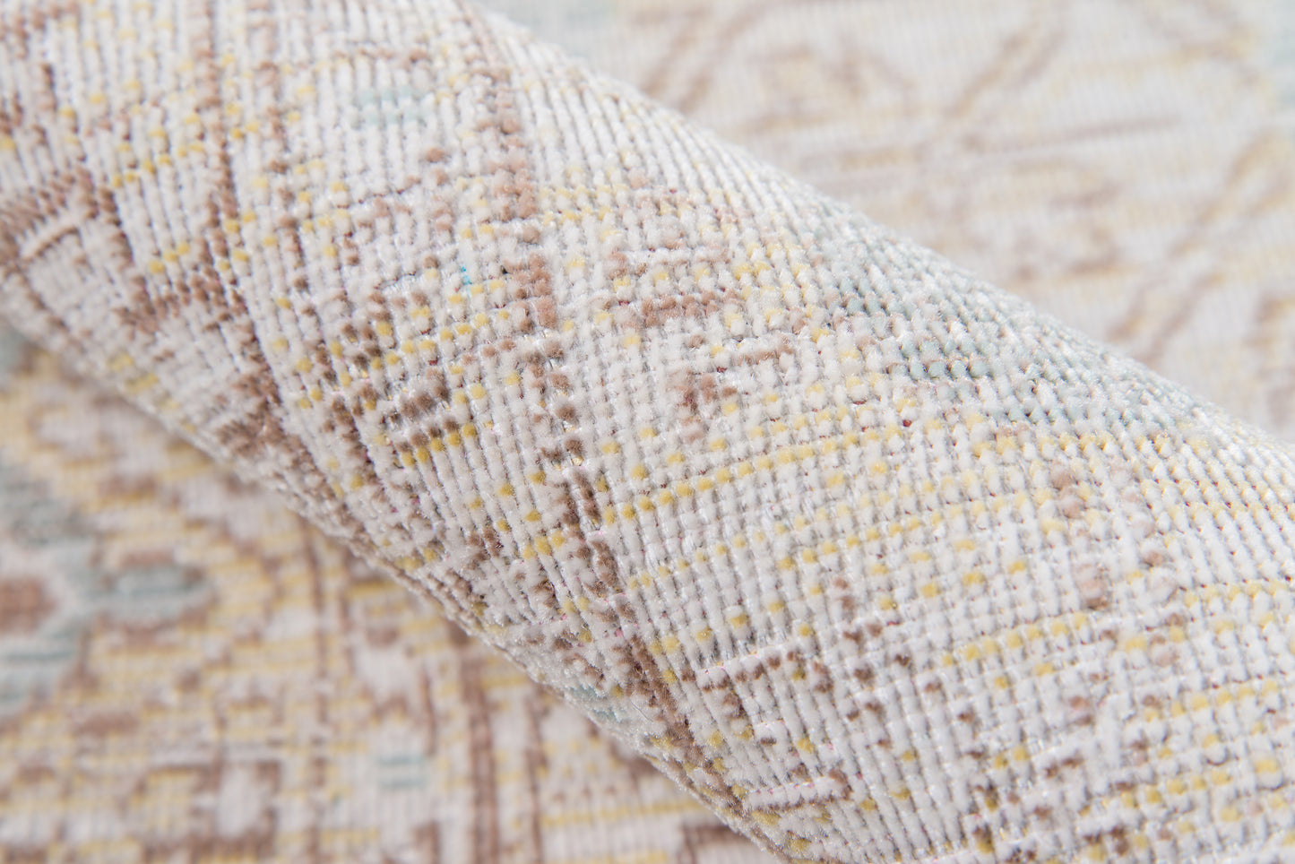 Close-up of beige woven rug with pale blue and yellow specks, textured geometric pattern, rolled edge.