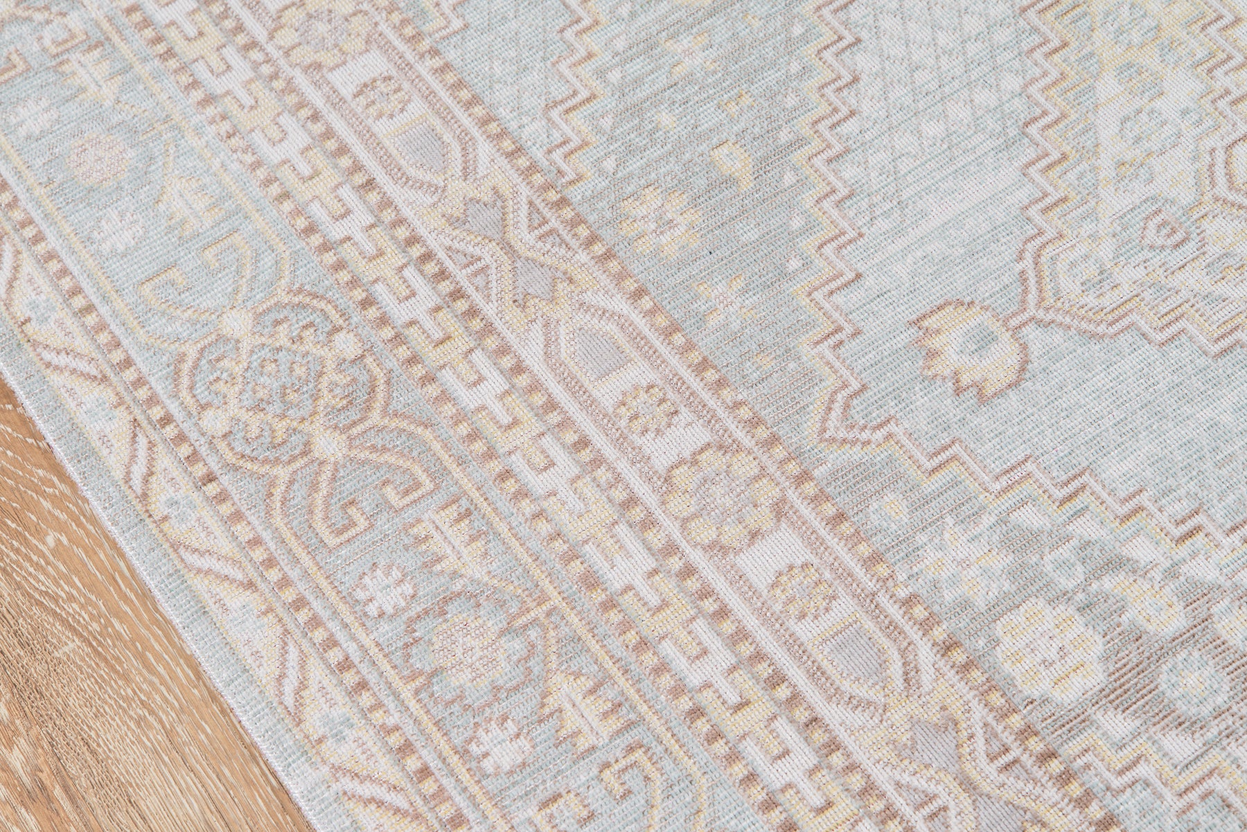 Rectangular rug with pale blue, ivory and beige tones, ornate geometric floral border on a wooden floor.
