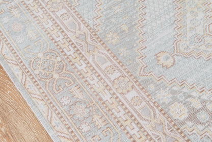Rectangular rug with pale blue, ivory and beige tones, ornate geometric floral border on a wooden floor.