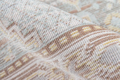 Close-up of a woven rug in soft beige with blue and yellow geometric pattern; textured fabric.