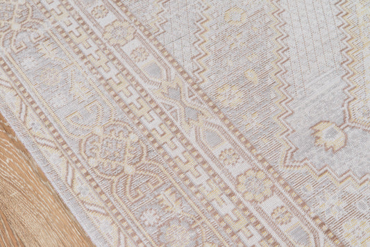 Grey & beige ornamental rug with floral and geometric border on a wooden floor.