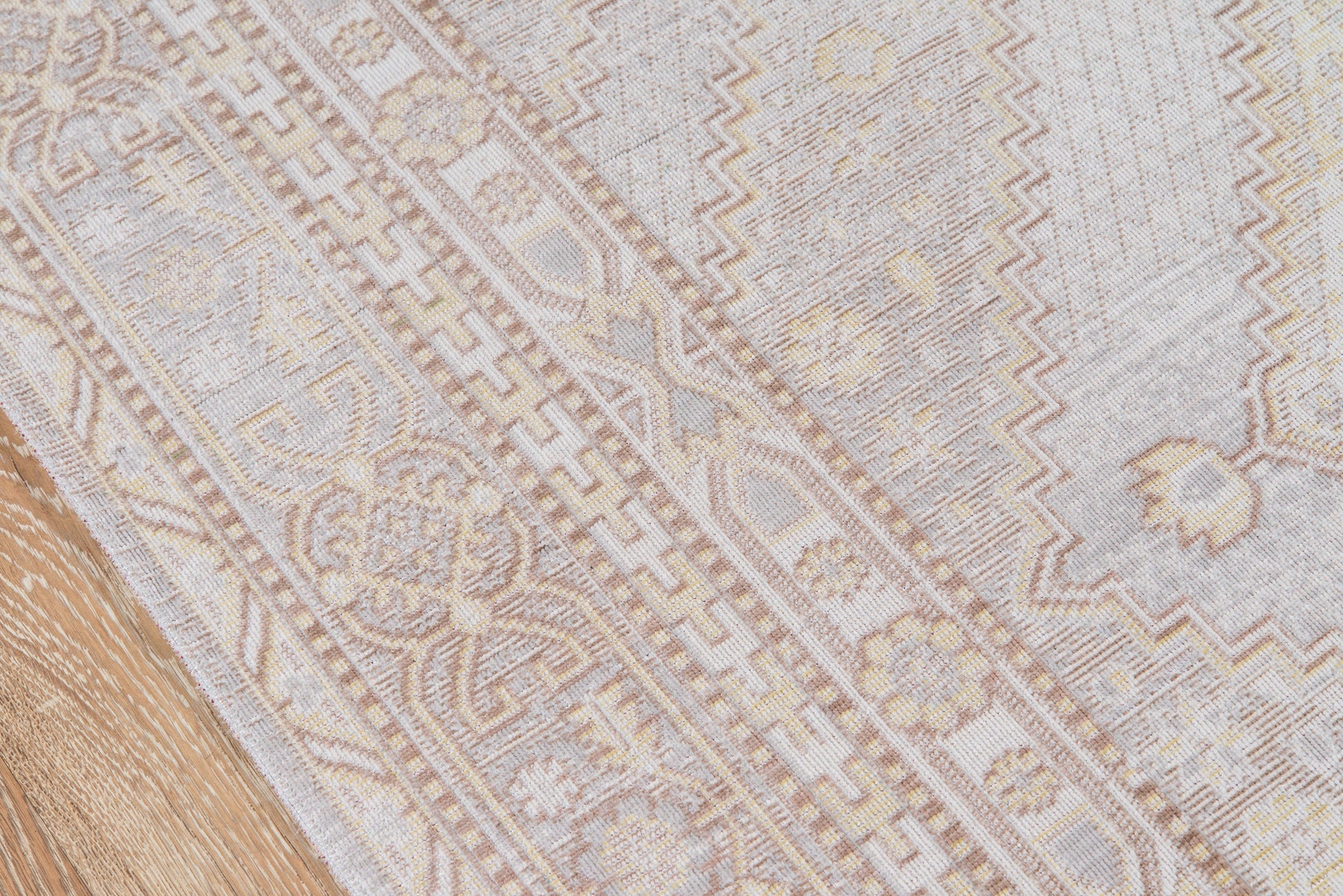Gray and cream oriental-style rug with floral motifs and geometric borders on hardwood floor.