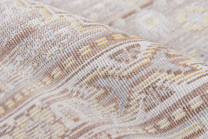 Close-up of a woven kilim rug in beige, ivory and taupe with geometric diamond motifs and subtle yellow accents.