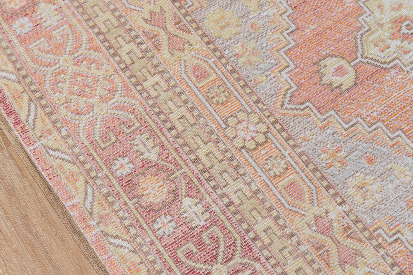 Woven oriental area rug in pink, peach, cream and beige with floral and geometric borders on a wooden floor.