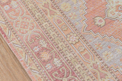 Woven oriental area rug in pink, peach, cream and beige with floral and geometric borders on a wooden floor.