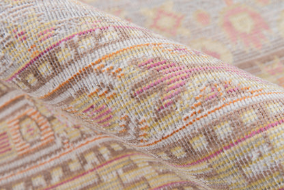 Close-up of a pastel geometric woven rug with pink, orange, cream tones; kilim-style bands and textured loom weave.