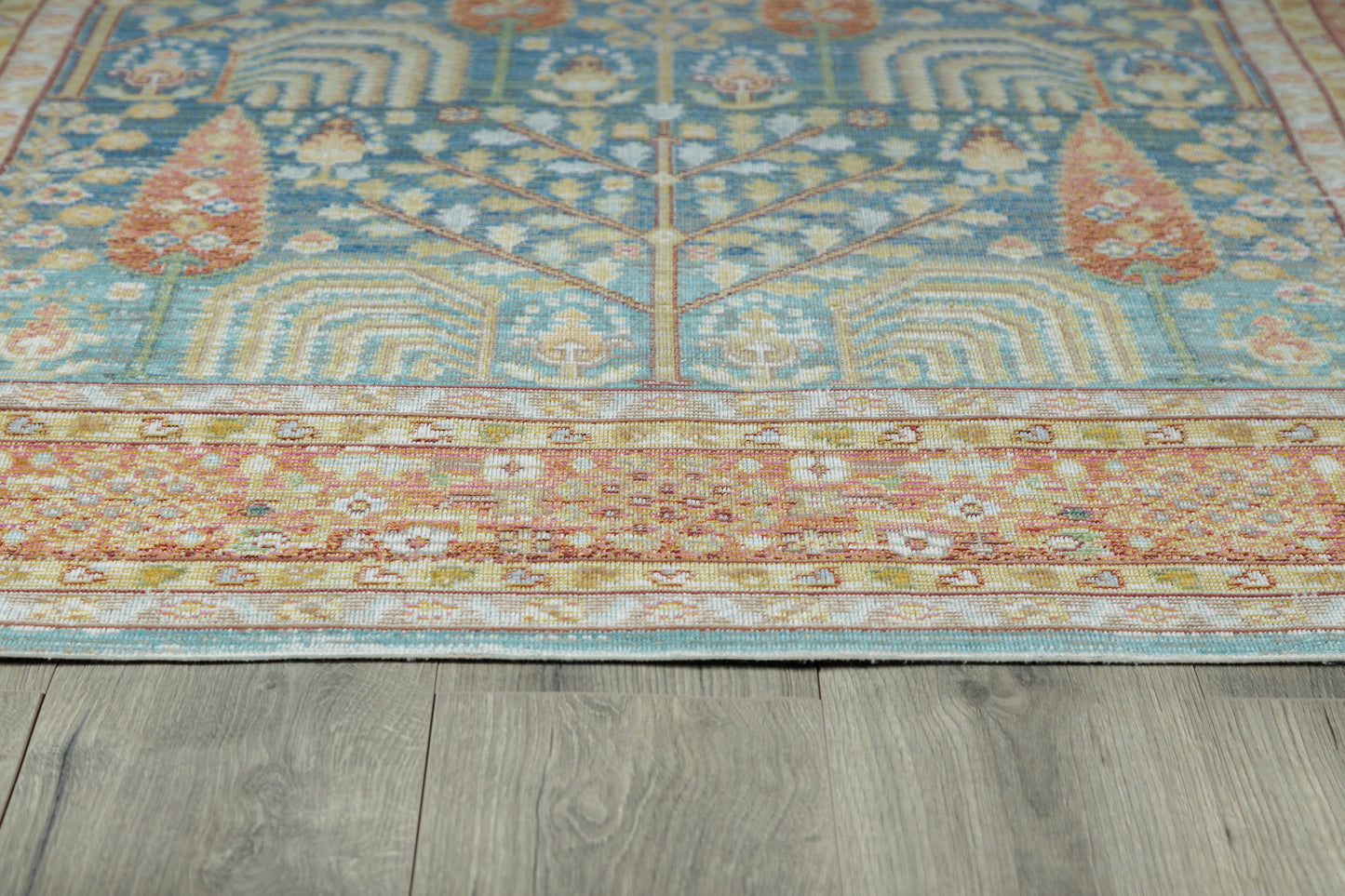 Blue oriental rug with cream floral motifs and a rust-red border on gray wood floor.